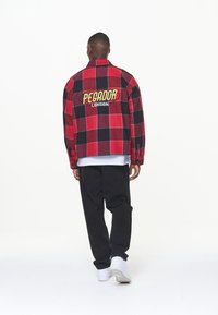 Czerwona i czarna flanelowa kurtka w kratę z wyszywanym na plecach napisem „PEGADOR LONDON”; zestawiona z czarnymi spodniami i białymi trampkami.