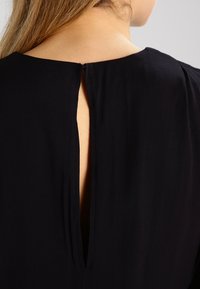 Svart klänning med en nyckelhålsöppning bak. Tyget verkar mjukt och slätt, med en enkel, svalande design utan utsmyckningar.