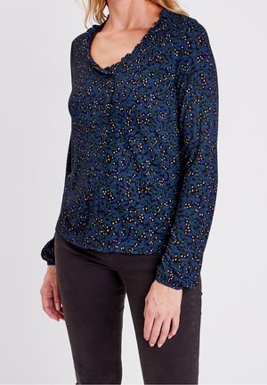 Blouse à manches longues en tissu bleu marine, présentant un motif floral avec des feuilles vertes et de petits pois blancs, ainsi qu'un col festonné.