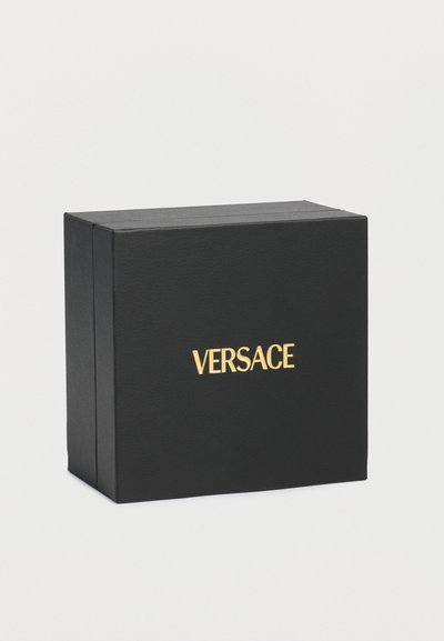 Μαύρο ορθογώνιο κουτί με χρυσό λογότυπο VERSACE στο κέντρο της εμπρόσθιας όψης, τοποθετημένο σε απλό ανοιχτό γκρι φόντο.