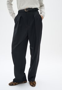 Pantaloni neri plissettati con vita alta, caratterizzati da una gamba larga e una cintura nera con una fibbia dorata. Abbinati a ballerine con stampa leopardata.