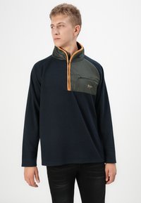 Pullover in pile di colore blu navy con una tasca sul petto con zip verde e dettagli arancioni. Presenta un colletto alto e maniche lunghe. Texture liscia.