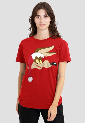 Woman wearing a red T-shirt with a cartoon coyote face wearing a red Santa hat, standing against a plain light gray background.