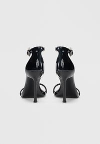 Sandalias de tacón alto de charol negro con tiras en el tobillo, que presentan un diseño elegante, puntera abierta y un detalle decorativo de hebilla.