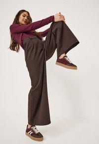 Kahruma garšam piegriezuma krekls ar garām piedurknēm apvienots ar augstās jostasvietas brūnām platām biksēm un kahruma krāsas sporta apaviem ar baltām šņorēm un teksturētu brūnu zoli.