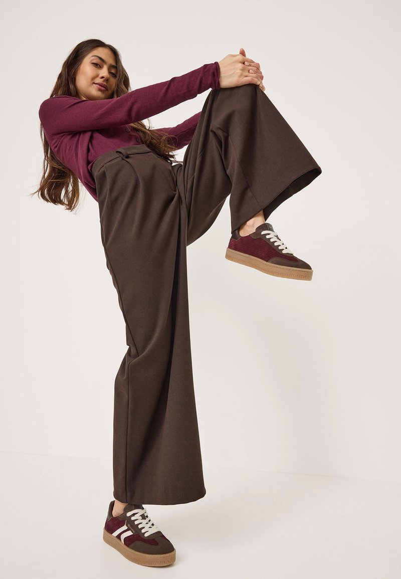 Kahruma garšam piegriezuma krekls ar garām piedurknēm apvienots ar augstās jostasvietas brūnām platām biksēm un kahruma krāsas sporta apaviem ar baltām šņorēm un teksturētu brūnu zoli.