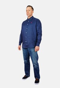 Navyblauw overhemd met lange mouwen, gemaakt van lichtgewicht stof, gecombineerd met blauwe denim jeans en zwarte schoenen met bruine veters.