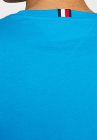 T-shirt in cotone turchese con design a V e un accento a righe sulla parte posteriore del collo, caratterizzato da una texture liscia e uniforme.