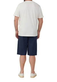 Men's white cotton t-shirt with short sleeves, paired with navy pleated shorts. The outfit is completed with light-colored sneakers.