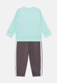Sudadera verde menta de manga larga y cuello redondo, combinada con pantalones de chándal gris oscuro que presentan franjas laterales blancas y puños elásticos.