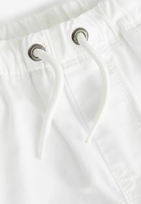 Shorts en coton blanc avec une fermeture à cordon et une texture lisse, dotés d'œillets en métal pour plus de durabilité. Le design est simple et fonctionnel.
