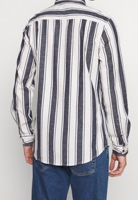 Camicia a maniche lunghe con bottoni, a righe verticali blu e bianche, realizzata in un tessuto leggero. Presenta un orlo curvo e polsini con bottoni.