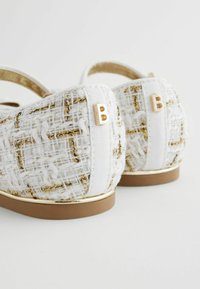 Weiße und goldene flach gewebte Schuhe mit einer strukturierten Oberfläche, die ein goldenes Akzent auf der Ferse und eine flexible, dünne Sohle aufweisen.