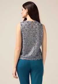 Top senza maniche argento con motivo a scallop e dettagli in paillettes, con apertura a chiave sul retro, abbinato a pantaloni teal.