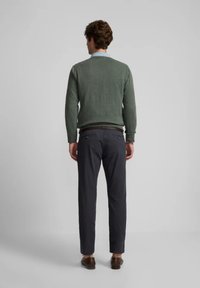 Suéter verde de punto combinado con pantalones oscuros, visto desde la espalda. El suéter tiene un escote acanalado y los pantalones tienen bolsillos.