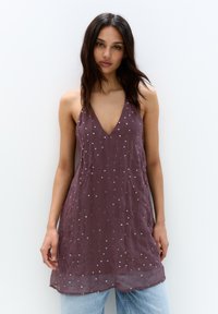 O rochie fără mâneci, de culoare prune, cu un decolteu adânc în V, realizată dintr-un material ușor, decorat cu modele de puncte argintii.