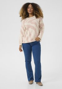 Ljust rosa och krämfärgad tröja med ett vågigt mönster, kombinerad med blå utsvängda jeans och beige skor. Mjuk textur och avslappnad passform.