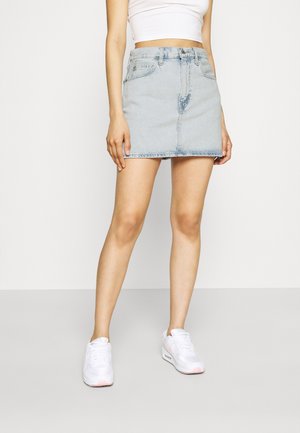 Jasnoniebieska mini spódnica dżinsowa o prostym kroju, z przednimi kieszeniami i widocznymi przeszyciami, zestawiona z białymi trampkami.