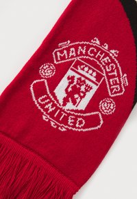 Raudona megzta šalikas su Manchester United logotipu baltai, su kutais apačioje ir juodu akcentu viename gale.