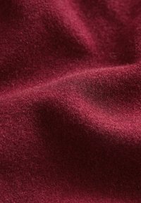 Țesătură de lână burgundă, cu o textură moale și o ușoară strălucire, având pliuri delicate și o încărcătură uniformă și densă.