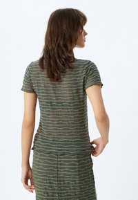Top de manga corta en color verde oliva con una tela transparente y texturizada que presenta un patrón ondulado, acompañado de una falda a juego.