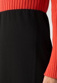 Knit dress with a ribbed red top and a fitted black skirt, featuring contrasting textures and colors that create a two-tone effect.