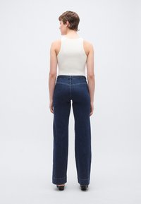 Τζιν παντελόνι από σκούρο μπλε denim με ψηλή μέση και φαρδιά πόδια, με κλείσιμο με φερμουάρ και κουμπί, και ελάχιστες ραφές. Απλό λευκό αμάνικο τοπ.