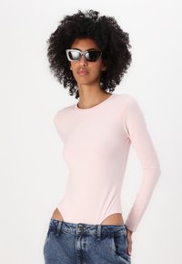 Roža dolg rokav bodi z oprijetim dizajnom, ki ima okroglo izreznico in GUESS JEANS logo; v kombinaciji z visokoraslimi denim šortkami.