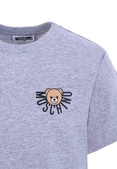 T-shirt en coton gris arborant un graphique d'ours brun avec un design en rayon de soleil et le mot "MOSCHINO" en noir, col rond et manches courtes.
