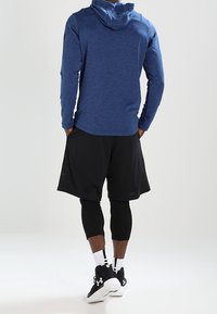 Felpa sportiva con cappuccio blu, pantaloni corti in rete neri, leggins neri aderenti, calze bianche e sneaker nere. Tessuto liscio, vestibilità atletica.