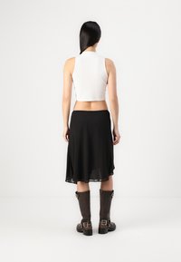 Biely, bezrukávový crop top a čierna, priestranná midi sukňa. Hnedé čižmy po kolená s prackami. Hladké textúry a minimalistický dizajn.