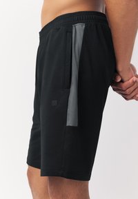 Fekete atlétikai rövidnadrág könnyű anyagból, szürke oldalsó betéttel, rugalmas derékrésszel és két oldalzsebbel tároláshoz.