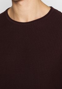 Bordowy sweter z teksturowanym, prążkowanym wzorem. Posiada okrągły dekolt i miękką, tkana tkaninę dla komfortu.