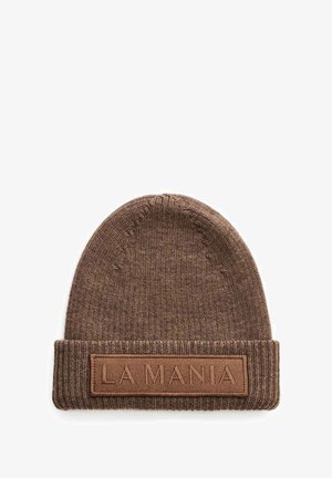 Brączowy dzianinowy beanie z zagiętym mankietem, na którym znajduje się prostokątna skórzana naszywka z wytłoczonym napisem "LA MANIA" na białym tle.