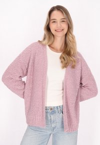 Ljusrosa, strukturerad cardigan med öppen front och ribbad nederkant; buren över en vit, figurnära topp och matchad med ljusblå jeans.