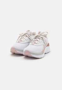 Chaussures de sport comprenant un mélange de tissu en maille blanc et rose clair, une semelle en caoutchouc texturée et des détails contrastants sur le talon.