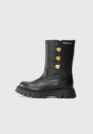 Stivaletto in pelle nera con accenti hardware a forma di orso dorato, cerniera laterale e suola nera chunky a coste.