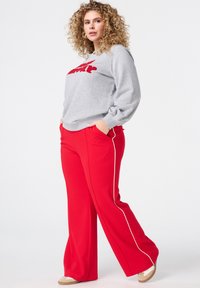 Gray sweatshirt with red lettering, paired with red sweatpants featuring white side stripes. Soft fabric, relaxed fit, and tapered leg design.