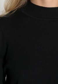 Zwarte geribbelde trui met een hoge kraag, voorzien van een getextureerde stof en een nauwsluitend ontwerp, zonder zichtbare hardware of patronen.