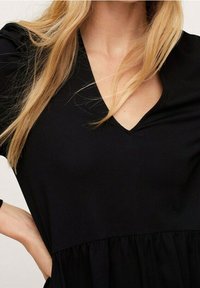 Robe noire avec décolleté en V, manches courtes et jupe froncée. Fabriquée à partir d'un tissu lisse, elle présente une coupe décontractée et une silhouette fluide.