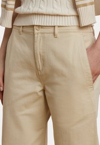 Pantaloni din bumbac bej cu croi drept, având închidere cu nasture, buzunare laterale și un material texturat. Design simplu și curat.