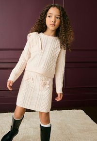 Gaiši rozā adīta apģērba komplekts ar ziloņu rakstu, garām piedurknēm ar ribota apdari un svārkiem ar lentīšu akcentiem. Apvienots ar melnu augstās potītes apavu komplektu.