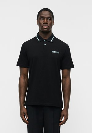 Mand iført sort Just Cavalli polo-shirt med lyseblåt logo og kravekant, stående mod en ensfarvet hvid baggrund.