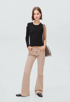 Schwarzes Langarmshirt mit einem Schulterauschnitt, kombiniert mit beigen Schlagjeans und schwarzen Ballerinas. Neutrale Handtasche über der Schulter getragen.