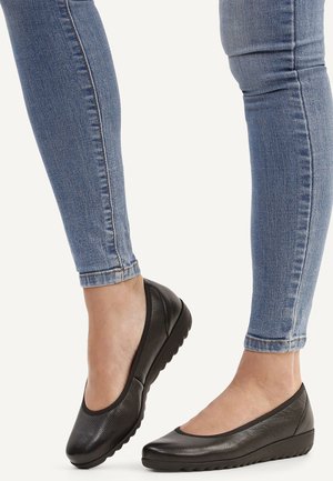 Black leather ballet flats with a rounded toe and flexible rubber sole, worn with blue skinny jeans. The upper has a textured finish.