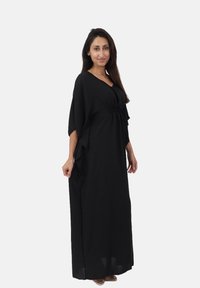 Robe maxi noire avec un design fluide, des manches courtes, une taille cintrée et un tissu texturé, dotée d'un décolleté en V et de fentes sur les côtés.