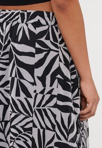 Black and white skirt featuring a leaf pattern, made of lightweight fabric. Elastic waistband with a textured finish and side detailing.