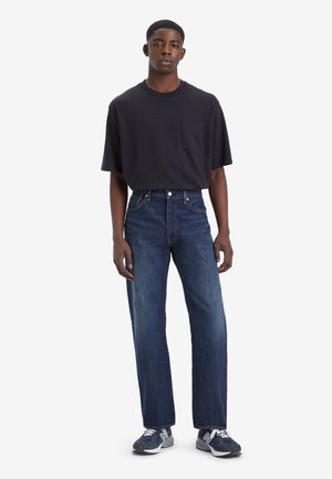 Black short-sleeve t-shirt with pocket, paired with straight-leg dark blue jeans and gray athletic shoes with white accents.