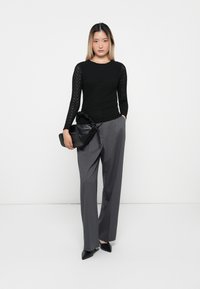 Black textured long-sleeve top paired with high-waisted gray wide-leg trousers and a black leather handbag with a gathered detail.