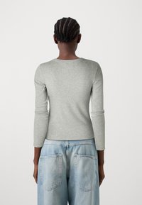 Graues langärmliges T-Shirt aus weichem Material, mit rundem Ausschnitt und tailliertem Design, kombiniert mit hellblauen hochtaillierten Jeans.